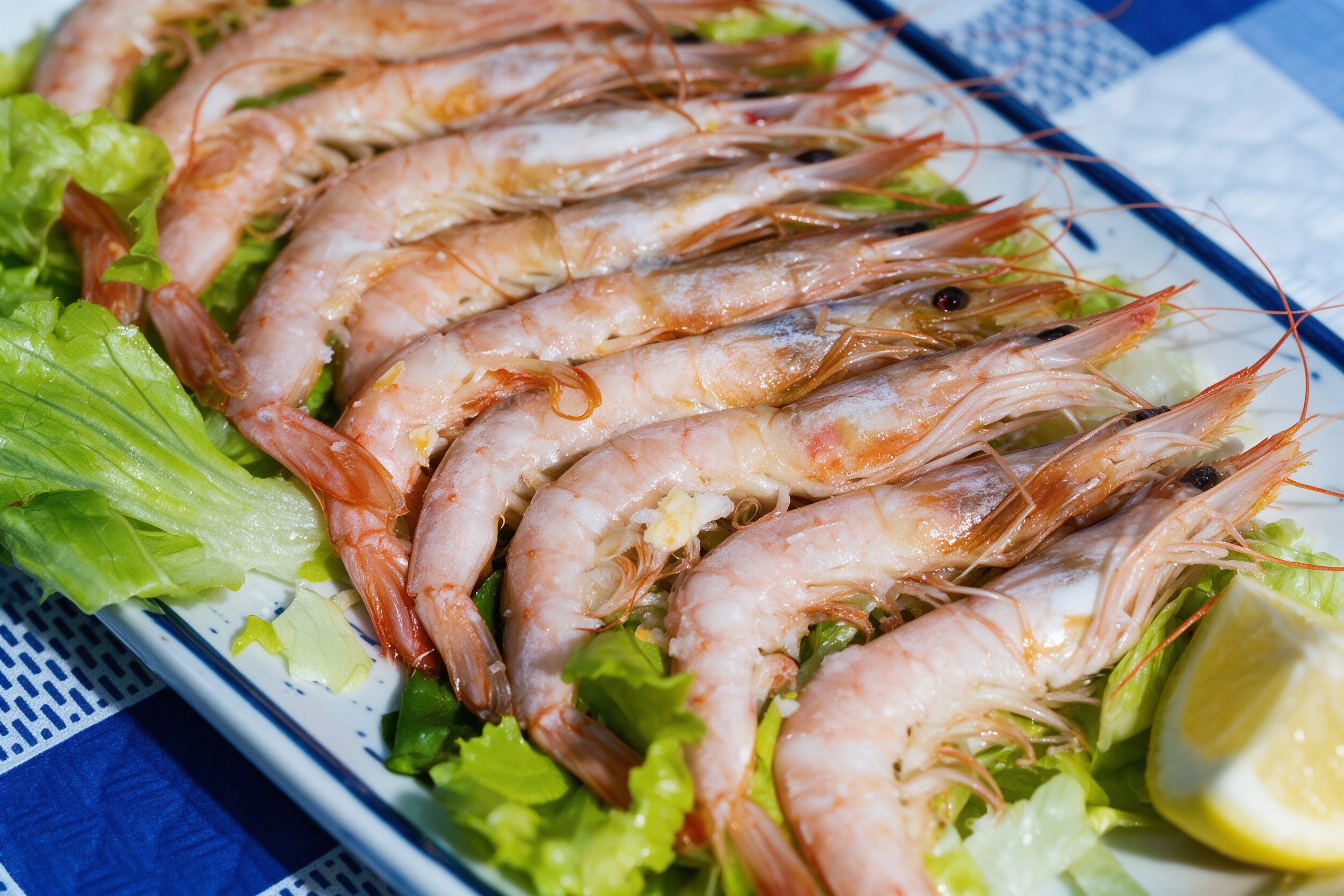 Filera de langostinos grandes con cabeza y cáscara sobre lechuga y limón en plato blanco